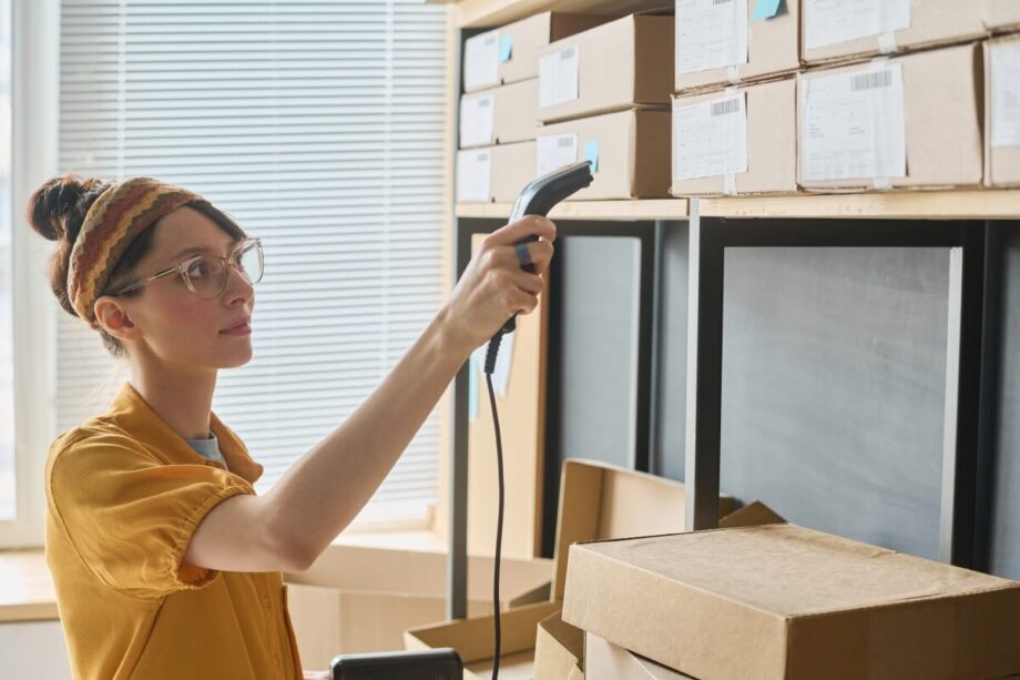 Kobieta używa skanery kodów kreskowych do skanowania pudełek w magazynie.