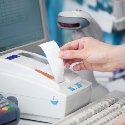 Ręka wyciąga paragon z drukarki fiskalnej przy kasie.