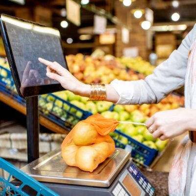 W sklepie spożywczym klientka waży owoce na wagi elektroniczne.